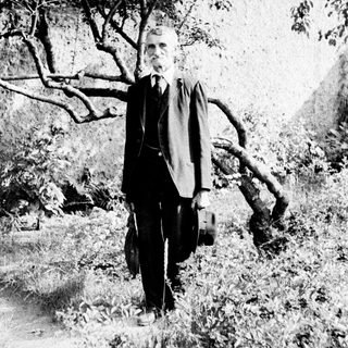 Man in suit stands outdoors with a briefcase.