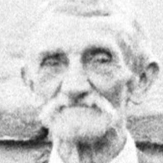 Elderly man in suit stands outdoors with a briefcase.
