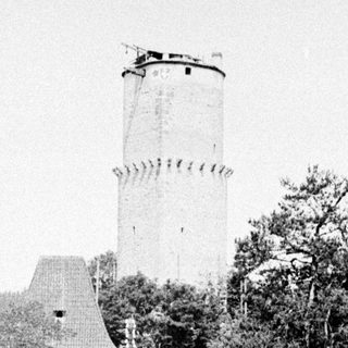 Man and woman walking near a tower and foliage.