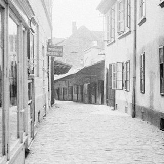 Here's a brief summary of the image: Narrow, cobbled street flanked by tall, old buildings.
