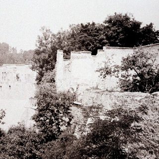 Ruined stone castle perched on a hillside, overgrown with foliage.