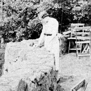 Man stands near a wall with chairs and foliage.