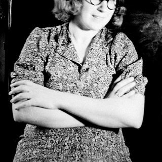 Here's a brief summary of the image: Woman in patterned shirt stands with arms crossed.