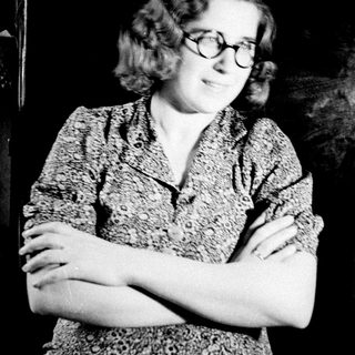Here's a brief summary of the image: Woman in patterned shirt stands with arms crossed.