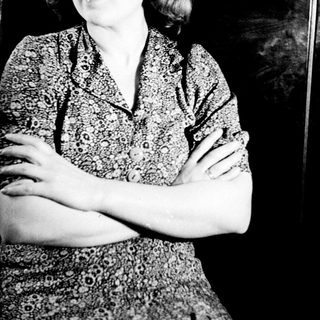 Here's a brief summary of the image: Woman in patterned dress stands with arms crossed.