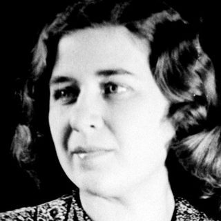 Here's a brief summary of the image: Woman in patterned dress stands with arms crossed.