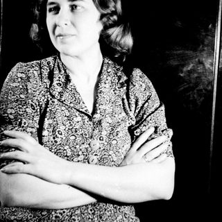 Here's a brief summary of the image: Woman in patterned dress stands with arms crossed.