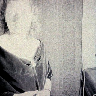 Here's a brief summary of the image: Portrait of a woman in historical dress, seated indoors.