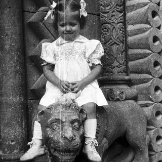 Here's a brief summary of the image: Young girl sits on a stone lion statue.