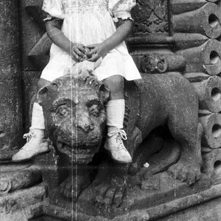 Here's a brief summary of the image: Young girl sits on a stone lion statue.