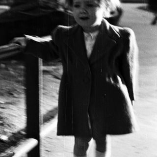 Young child stands outdoors, leaning on a railing.