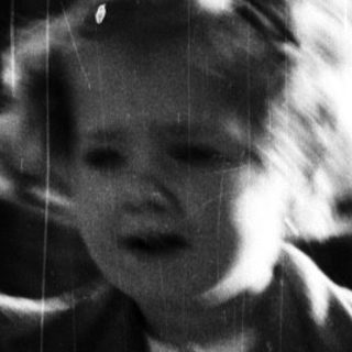 Young child stands outdoors, leaning on a railing.