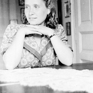 Woman sits at a table with hands clasped.