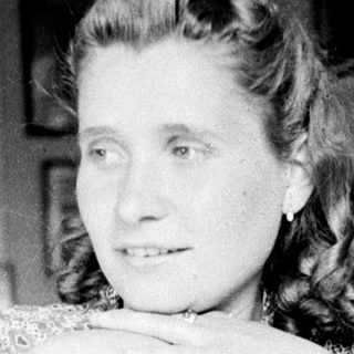 Woman sits at a table with hands clasped.