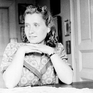 Woman sits at a table with hands clasped.