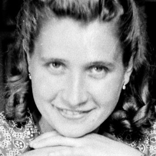 Woman with patterned dress smiles while seated at a table.