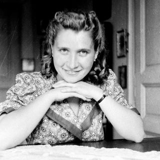 Woman with patterned dress smiles while seated at a table.