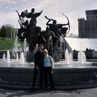 Couple poses in front of a fountain and statue.