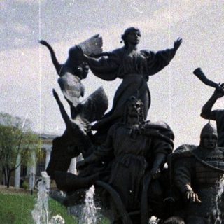 Couple poses in front of a fountain and statue.