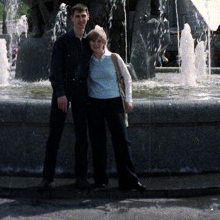 Couple poses in front of a fountain and statue.