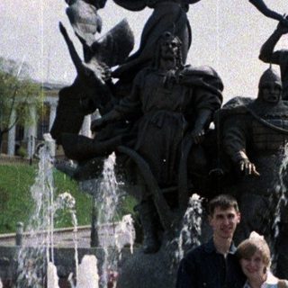 Couple poses in front of a fountain and statue.