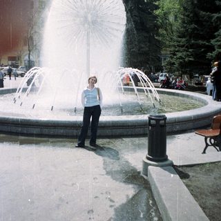 Woman stands near a fountain in a public park.
