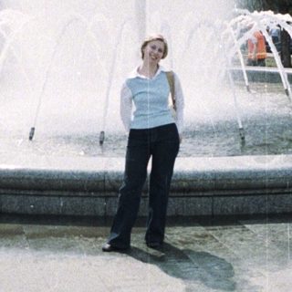 Woman stands near a fountain in a public park.