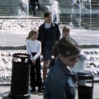 People stroll through a fountain plaza with architectural structures.