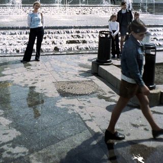 People stroll through a fountain plaza with architectural structures.