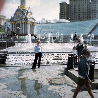 People stroll through a fountain plaza with architectural structures.