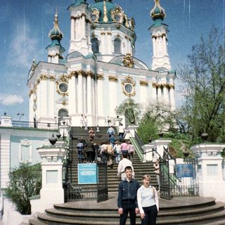 Two people stand before a large, ornate church building.
