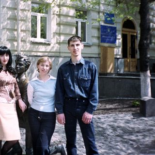 People posing near a statue in front of a building.