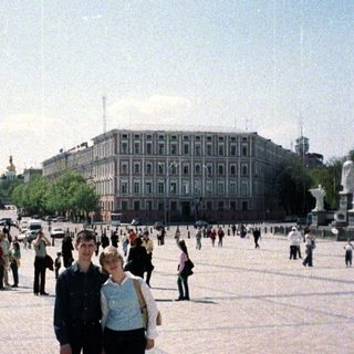 Couple stands in a square with a large building.