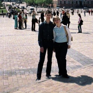 Couple stands in a square with a large building.