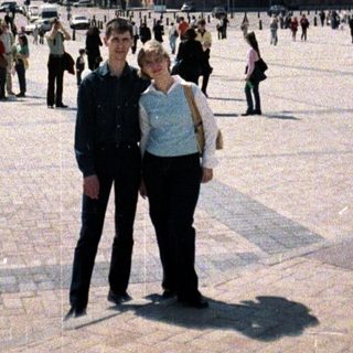 Couple stands in a square with a large building.