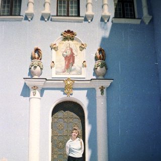 Woman stands before an ornate doorway and facade.