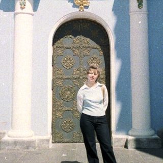Woman stands before an ornate doorway and facade.