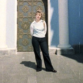 Woman stands before an ornate doorway and facade.