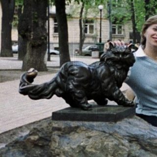 Woman posing near a statue of a cat on a rock.