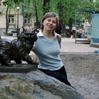 Woman posing near a statue of a cat on a rock.