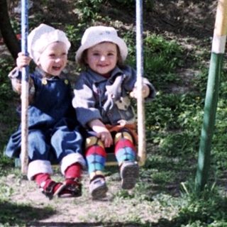 Two children sit on a swing set in a park.