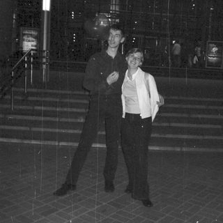 Couple stands outside a building in the rain at night.