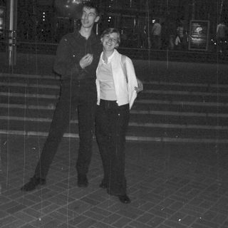 Couple stands outside a building in the rain at night.