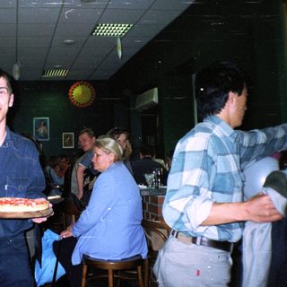 Man holds pizza in a bowling alley setting.