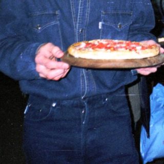 Man holds pizza in a bowling alley setting.