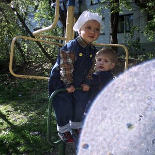 Boy in overalls plays on a playground apparatus outdoors.