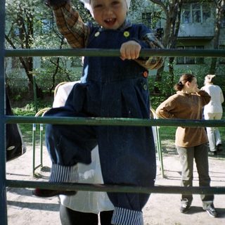 Here's a brief summary of the image: Girl playfully poses behind bars in an outdoor setting.