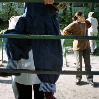 Here's a brief summary of the image: Girl playfully poses behind bars in an outdoor setting.