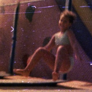 Girl sits on a slide, viewed through a fence.