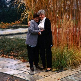 Two women stand near tall grass in a park.